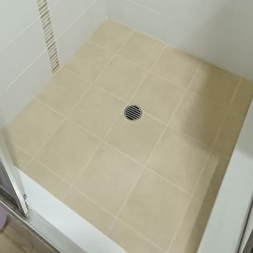 The same shower base after regrouting and resealing, with even grout lines across the tiled floor and clean white sealant at the wall junctions