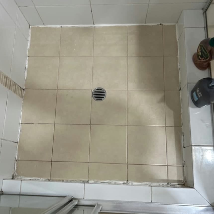 Shower base before regrouting and resealing, with blackened perished silicone along the junctions where the base meets the walls and discoloured grout across the tiled floor