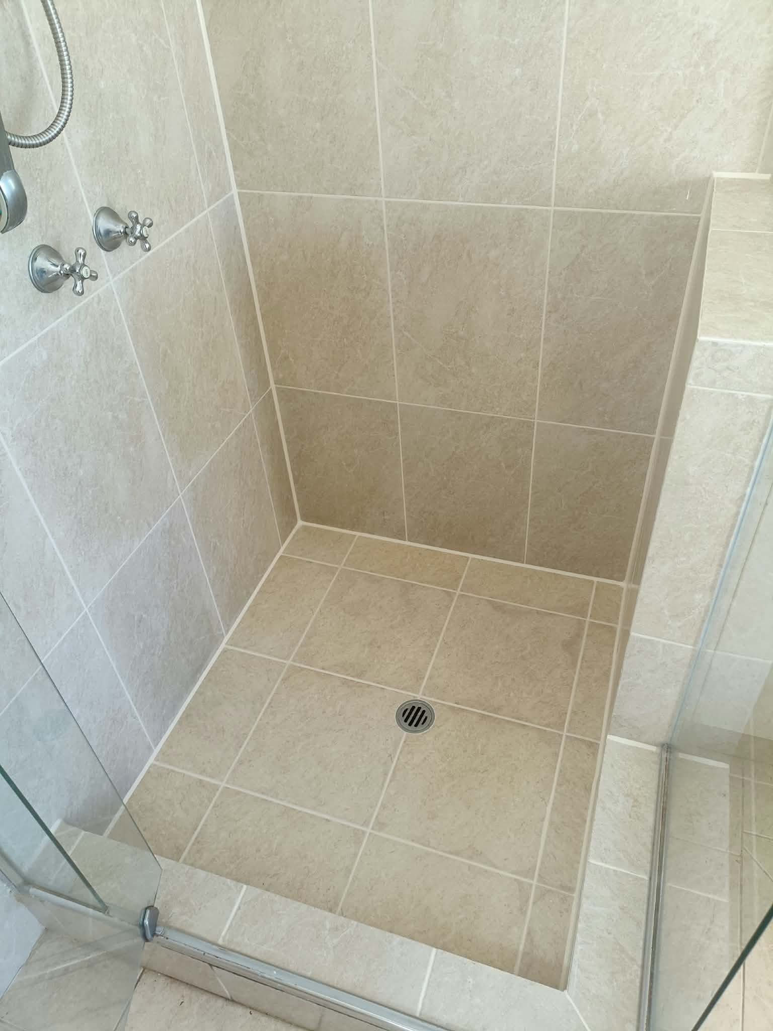 The same shower base after regrouting, with clean, even grout lines across the floor and a neat sealed joint at the wall