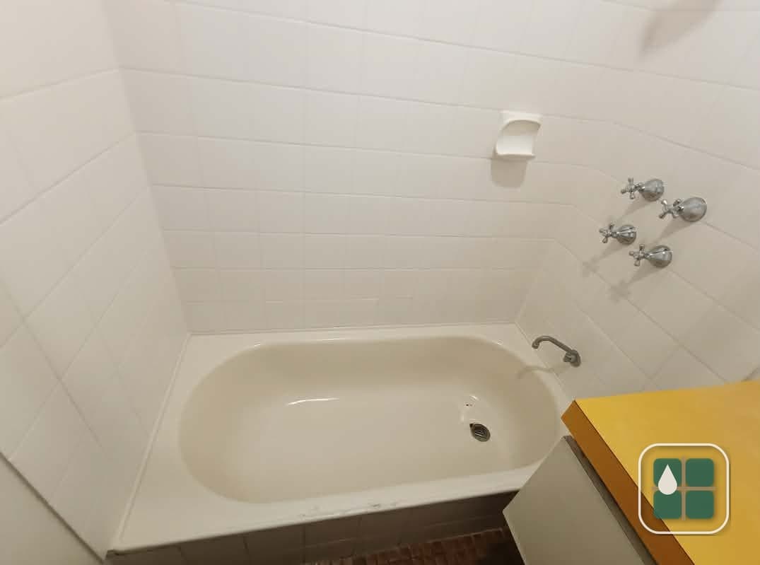 White tiled bath surround with a built-in soap recess and chrome tapware, the grout lines clean and the tile-to-bath junction sealed.