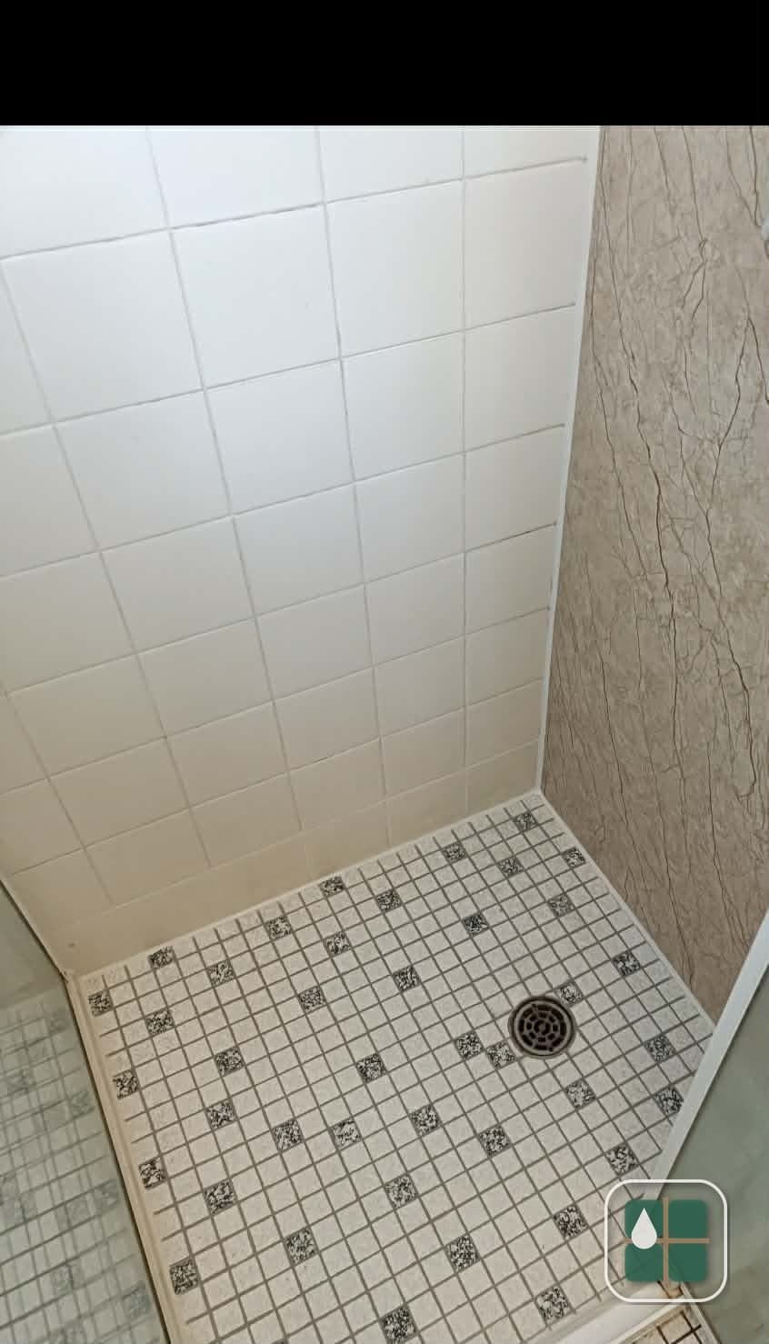 Corner of a shower recess with white square wall tiles and a speckled mosaic floor, all grout lines clean and consistent.